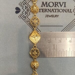 May include: Gold chain necklace with a variety of decorative links. The chain is measured against a ruler, showing it is approximately 1 inch long.