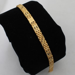 May include: A gold bracelet with a detailed, patterned design. The bracelet is made of linked, interlocking pieces.