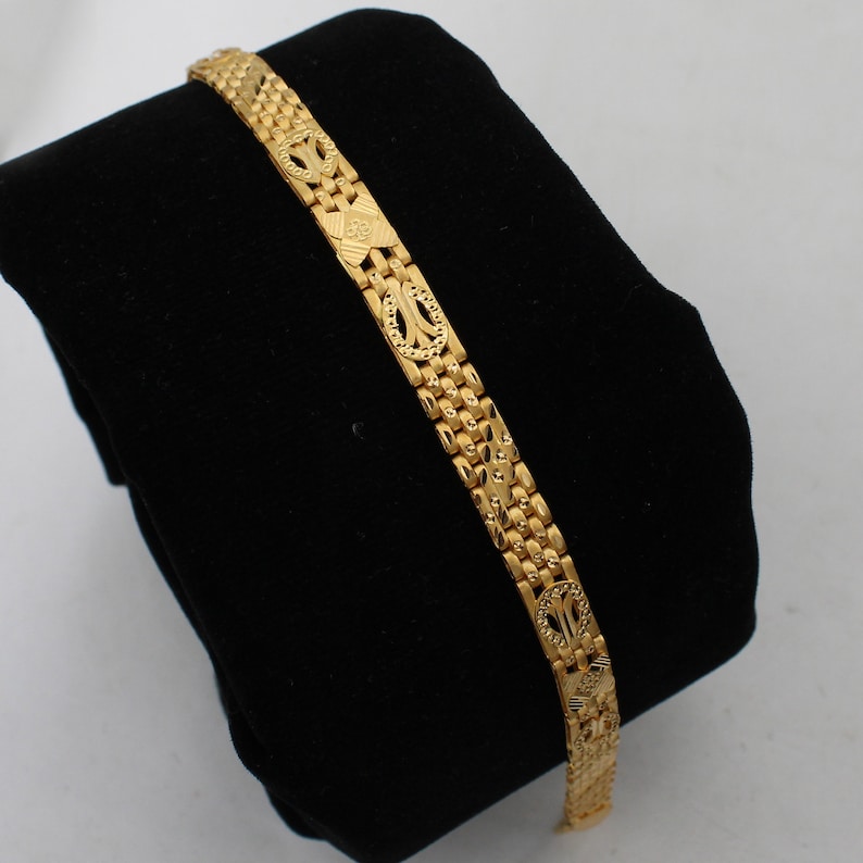 May include: A gold bracelet with a detailed, patterned design. The bracelet is made of linked, interlocking pieces.