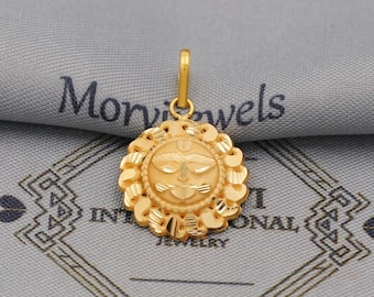 May include: A gold-colored pendant with a detailed sun-like design. The pendant features a central face with intricate patterns and is surrounded by a scalloped border. The pendant is suspended from a small loop.