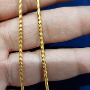 Puede incluir: Un collar de cadena de serpiente de oro. La cadena está hecha de pequeños eslabones entrelazados que crean un aspecto suave y fluido.