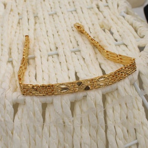 May include: A gold chain bracelet with a detailed, intricate design. The bracelet is made of multiple strands of gold chain, each with a different pattern. The chain is linked together to form a continuous loop.