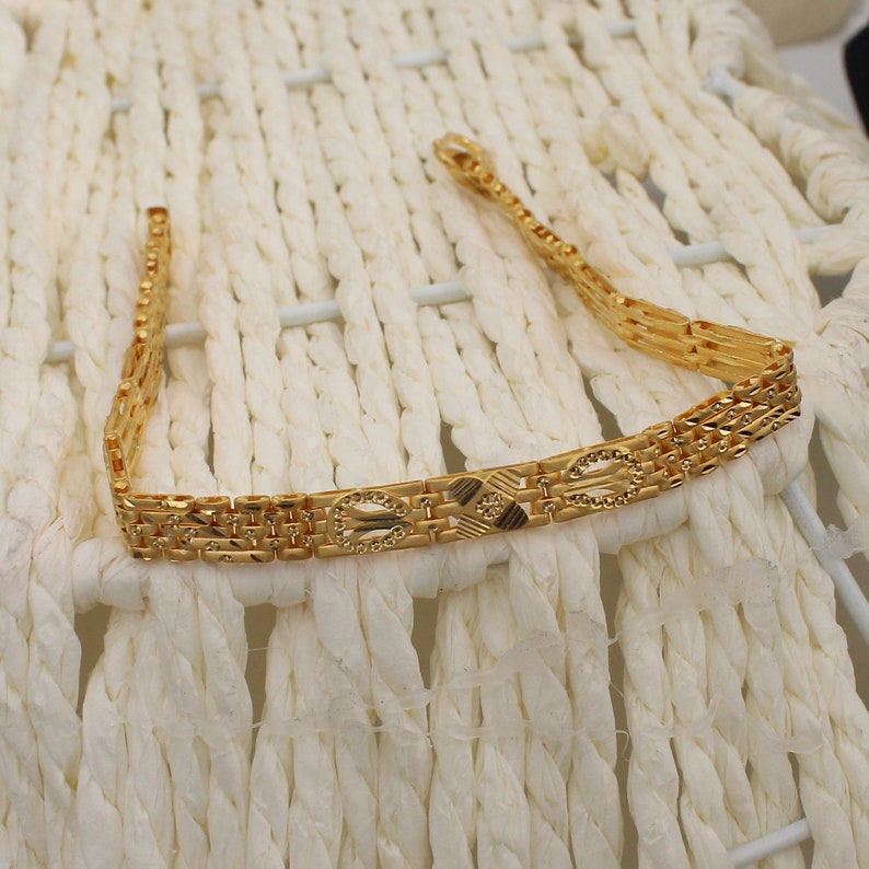 May include: A gold chain bracelet with a detailed, intricate design. The bracelet is made of multiple strands of gold chain, each with a different pattern. The chain is linked together to form a continuous loop.
