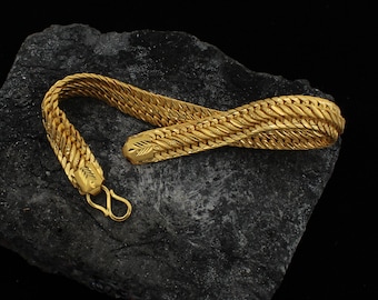 May include: A gold chain bracelet with a woven design. The bracelet is on a dark gray rock.