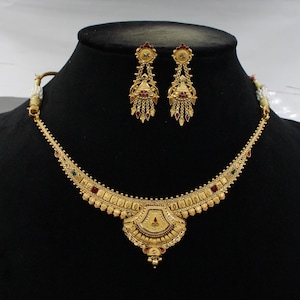May include: A gold necklace with a pendant and matching earrings. The necklace has a delicate chain with a central pendant that is shaped like a fan. The pendant is decorated with red, green, and gold stones. The earrings are also decorated with red, green, and gold stones.