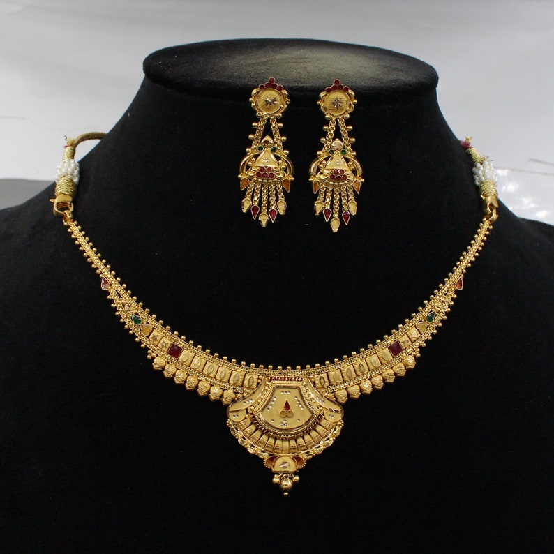 May include: A gold necklace with a pendant and matching earrings. The necklace has a delicate chain with a central pendant that is shaped like a fan. The pendant is decorated with red, green, and gold stones. The earrings are also decorated with red, green, and gold stones.