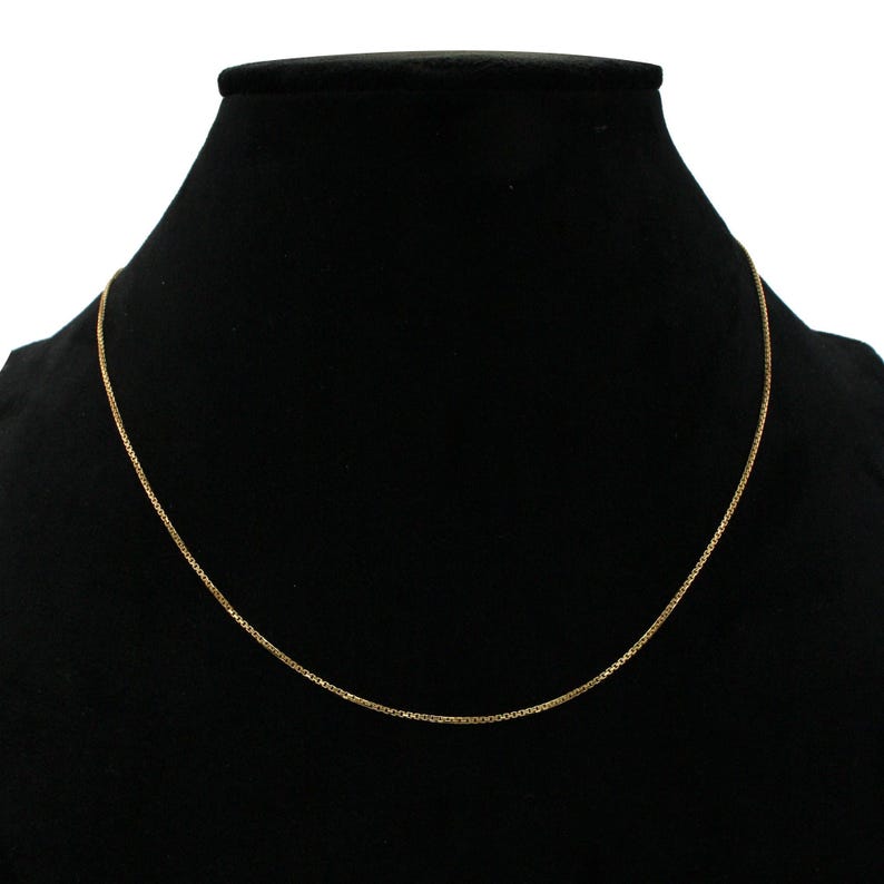 May include: A gold chain necklace on a black velvet display stand.