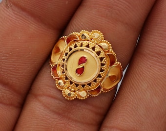 May include: A gold ring with intricate details and red accents. The ring features a circular design with a smaller circle in the center.