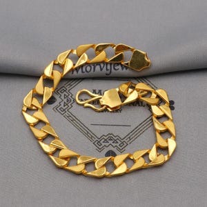 Puede incluir: Un brazalete de cadena de oro con cierre de gancho. El brazalete está hecho de eslabones redondeados entrelazados. El fondo es de color gris.