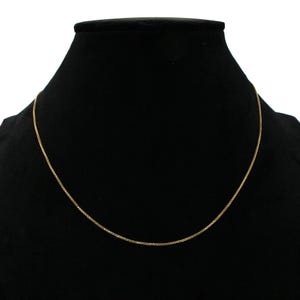 May include: A gold chain necklace on a black velvet display stand.