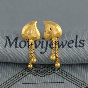 May include: A pair of gold earrings featuring a textured, leaf-shaped top section with a matte finish. Each earring has two delicate box chains hanging from the base, with a small, polished gold bead attached to the end of each individual chain.