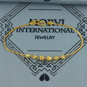 May include: A gold-colored bracelet with a delicate chain and a series of decorative beads. The bracelet features a hook clasp and is displayed against a blue background with the text "HORVI INTERNATIONAL JEWELRY".