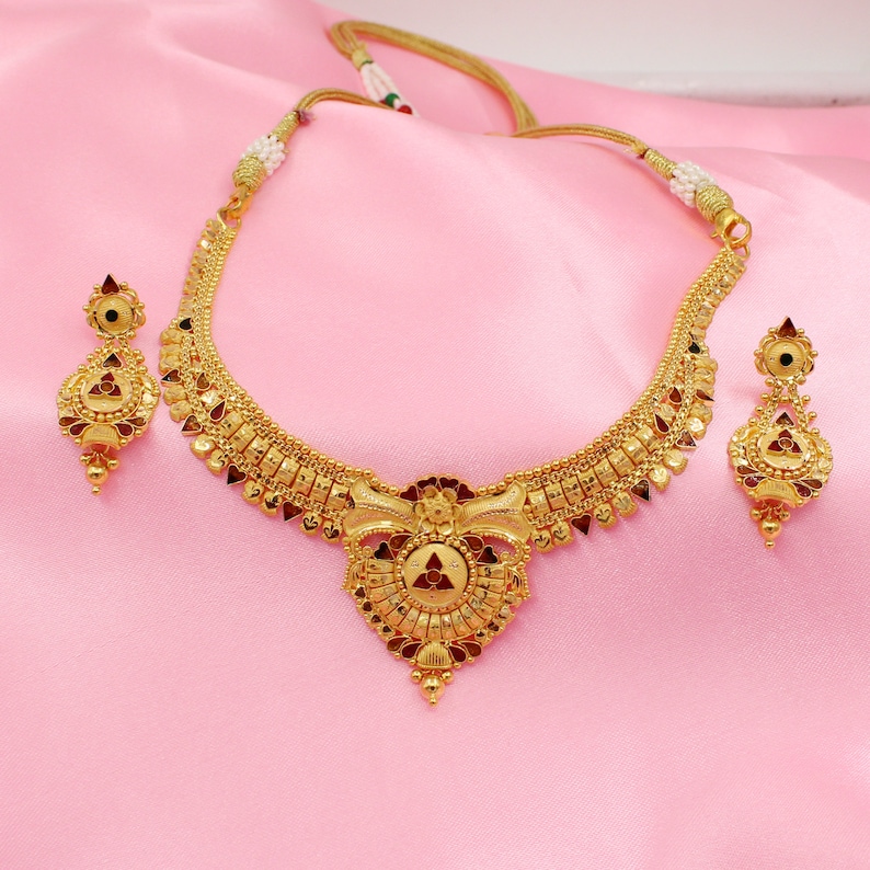 May include: A gold necklace and earrings set with a red and gold pendant. The necklace has a delicate chain and a detailed design with red stones.