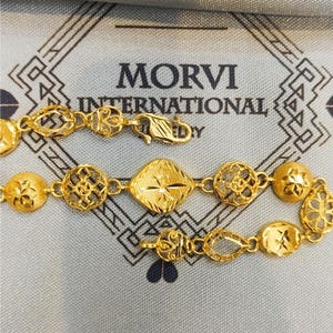May include: A gold bracelet with intricate designs. The bracelet features a variety of shapes, including circles, squares, and ovals. The bracelet is made of 22 karat gold and is a beautiful piece of jewelry.