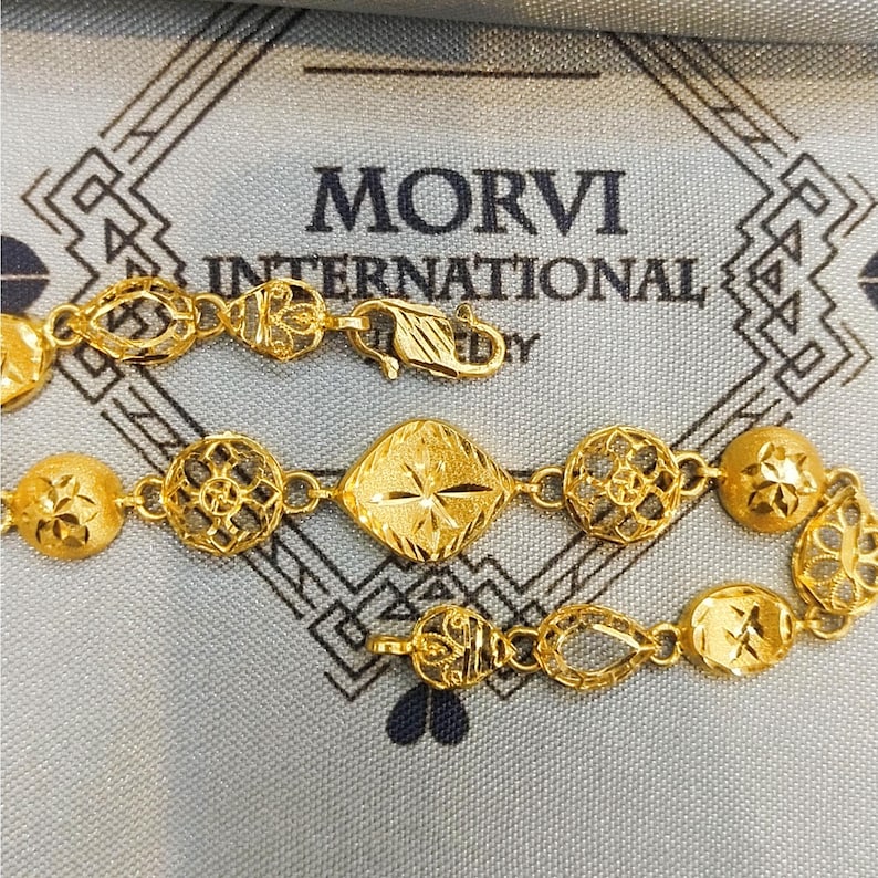 May include: A gold bracelet with intricate designs. The bracelet features a variety of shapes, including circles, squares, and ovals. The bracelet is made of 22 karat gold and is a beautiful piece of jewelry.