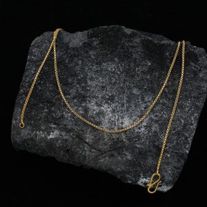 May include: A gold chain necklace with a box clasp. The chain is on a dark gray rock surface.