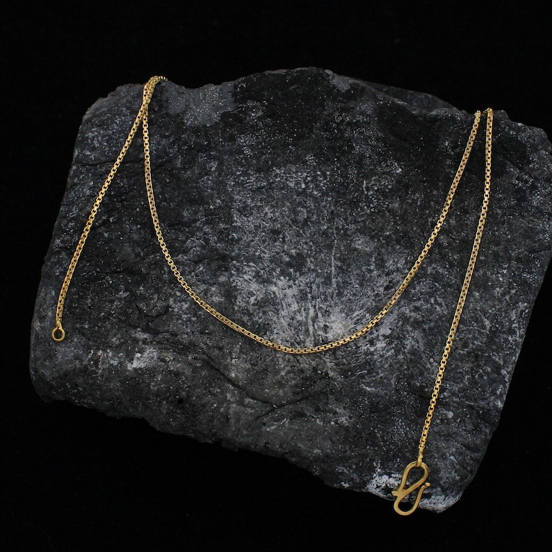 May include: A gold chain necklace with a box clasp. The chain is on a dark gray rock surface.