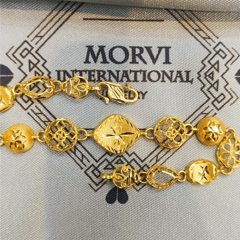 May include: A gold bracelet with intricate designs. The bracelet features a variety of shapes, including circles, squares, and ovals. The bracelet is made of 22 karat gold and is a beautiful piece of jewelry.