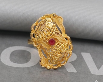 May include: A gold ring with intricate filigree detailing and a single red gemstone in the center.