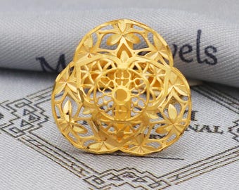 May include: A gold-colored ring with an openwork floral design. The ring features a three-lobed shape with intricate cut-out patterns. The ring is set against a gray and white patterned background.