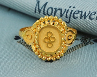 May include: A gold ring with a circular design featuring four interlocking circles. The ring has a decorative border and a textured surface.