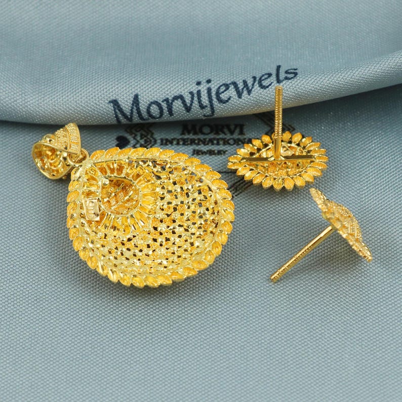 Op de afbeelding: Een set gouden oorbellen en een ketting met hanger. De oorbellen en hanger hebben een rond ontwerp met ingewikkeld filigraanwerk.