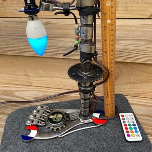 May include: A unique desk lamp crafted from repurposed metal components, including gears, wrenches, and engine parts. The lamp features a blue LED light bulb and stands approximately 12 inches tall. A remote control with multiple color options is included.
