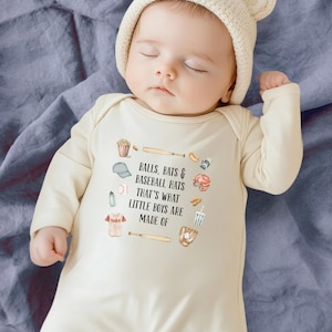 May include: A cream-colored baby gown with long sleeves features a baseball-themed design with the text "Balls, Bats & Baseball Hats That's What Little Boys Are Made Of". The gown is decorated with watercolor illustrations of baseball equipment, snacks, and drinks.