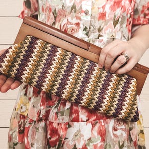 May include: A brown wooden framed clutch with a woven chevron pattern in shades of beige, brown, and purple.
