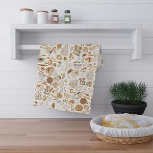 May include: A kitchen towel with a repeating pattern of baking tools and ingredients in shades of brown and beige. The towel hangs on a white shelf above a wooden countertop. A loaf of bread sits in a wicker basket.