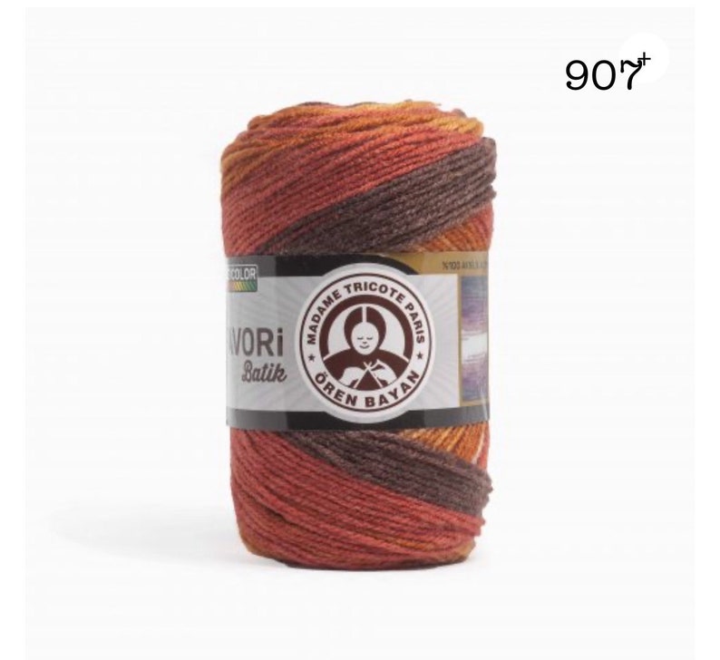 Puede incluir: Un ovillo de hilo "AVORI Batik" en tonos marr&oacute;n, naranja y rojo. La etiqueta presenta el texto "MADAME TRICOTE PARIS" y "&Ouml;REN BAYAN". El n&uacute;mero "907" es visible en la esquina superior derecha. El hilo est&aacute; bien enrollado.