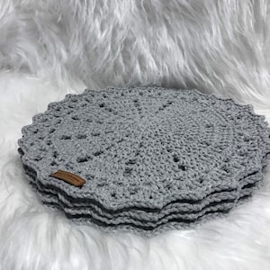 May include: A stack of gray crocheted placemats with a brown label that says "Handmade with Love".