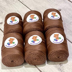 May include: Six spools of brown yarn are displayed. Each spool features a white sticker with a cartoon bear and the text "www.sydneyyarn.com.au". The yarn is tightly wound, and the colour is a rich, warm brown. Ideal for various crafting projects.