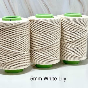 May include: Three spools of 5mm White Lily macrame cord. The cord is a creamy white colour, tightly wound around green spools. The text "5mm White Lily" is displayed at the bottom of the image.