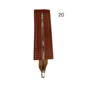 May include: A brown leather zipper with a silver metal pull. The leather has evenly spaced holes along the edges. The number 20 is in the upper right corner.