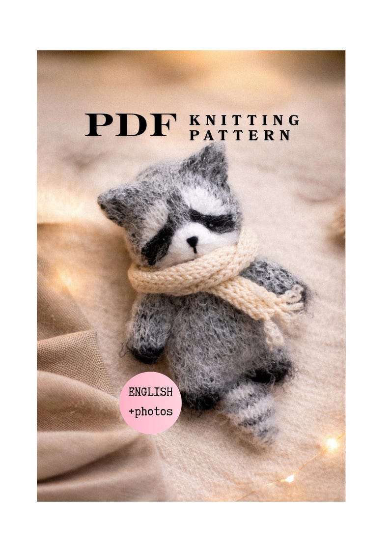 May include: A PDF knitting pattern for a small, fuzzy grey and white raccoon toy. The raccoon has black eye patches, a black nose, and wears a cream-coloured knitted scarf. The text reads PDF KNITTING PATTERN and ENGLISH +photos.