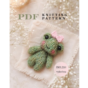 Peut inclure: Un modèle de tricot PDF représentant une petite grenouille tricotée à la main de couleur verte avec des yeux noirs, des joues roses et un petit nœud rose sur la tête. Le texte sur l'image indique PDF KNITTING PATTERN et ENGLISH +photos.
