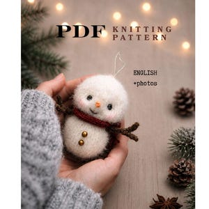 Op de afbeelding: Een PDF-breipatroon voor een kleine, handgemaakte sneeuwpop-ornament. De sneeuwpop is wit met een rode sjaal, bruine takarmen en gouden knoopdetails. De tekst "ENGLISH + photos" is ook zichtbaar.