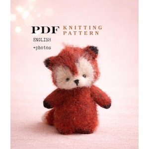 Pode incluir: Um brinquedo de pelúcia de raposa vermelha e branca feito à mão. A raposa tem uma aparência fofa e texturizada com detalhes pretos nas orelhas e patas. A imagem também inclui o texto "PDF Knitting Pattern English + photos".