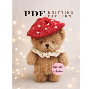 Op de afbeelding: Een gebreide teddybeer met een rode paddenstoelmuts met witte stippen en een crèmekleurige kanten kraag. De afbeelding bevat de tekst "PDF KNITTING PATTERN" en "ENGLISH + photos".
