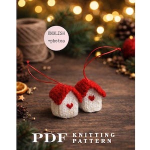 Op de afbeelding: Twee kleine gehaakte huisornamenten met witte muren en rode daken, elk met een klein rood hartje aan de voorzijde en een rood ophangkoord. Een label toont ENGLISH +photos en de tekst onderaan luidt PDF KNITTING PATTERN.