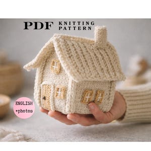 Può includere: Un modello di maglia in PDF per una piccola casa color crema con tetto testurizzato, camino e finestre e porta marrone chiaro. Il testo PDF KNITTING PATTERN è visibile in alto e un cerchio rosa con ENGLISH +photos è sulla sinistra.