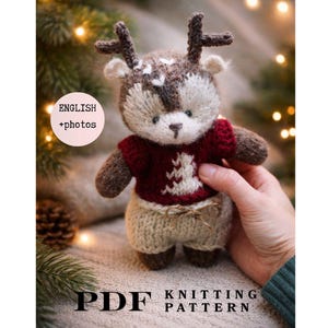 May include: A PDF knitting pattern featuring a small, hand-knitted reindeer toy with brown fur, dark antlers, a deep red jumper with a white tree design, and light beige trousers. The text "ENGLISH +photos" and "PDF KNITTING PATTERN" is visible.