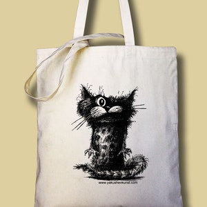 May include: A white canvas tote bag with a black and white illustration of a cat with a single large eye. The text "www.yakushevkunst.com" is printed on the bottom of the bag.