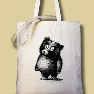 May include: A white tote bag with a black and white illustration of a bear with big eyes. The text "www.yakushevkunst.com" is printed on the bottom of the bag.