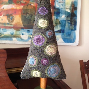 May include: A handcrafted, decorative Christmas tree with a dark gray textured exterior and colorful floral accents. The tree is mounted on a wooden stand with a green base. The tree is approximately 10 inches tall.