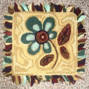 Peut inclure: Tapis carré fait à la main avec un motif floral. Le tapis présente une grande fleur avec des pétales turquoise et un centre marron, ainsi que des feuilles marron. La bordure est ornée de bords frangés colorés. Le fond est jaune clair.