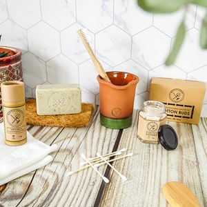 May include: A bathroom vanity with a variety of eco-friendly products, including a bar of soap, a toothbrush, a jar of cotton buds, and a tube of deodorant. The products are all made from natural materials and are packaged in sustainable packaging.