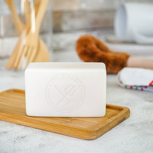 May include: A white bar of soap with a logo that says "Dirty Goblin" in a circle with a crossed trident inside. The soap is sitting on a wooden tray.