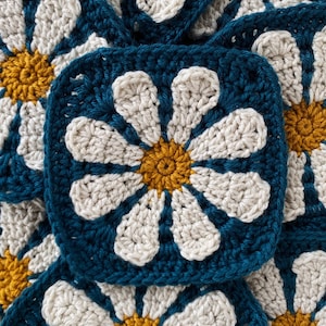 May include: Close-up of crocheted flower squares in teal, white and gold. The squares are made with a granny stitch pattern and feature a daisy design.
